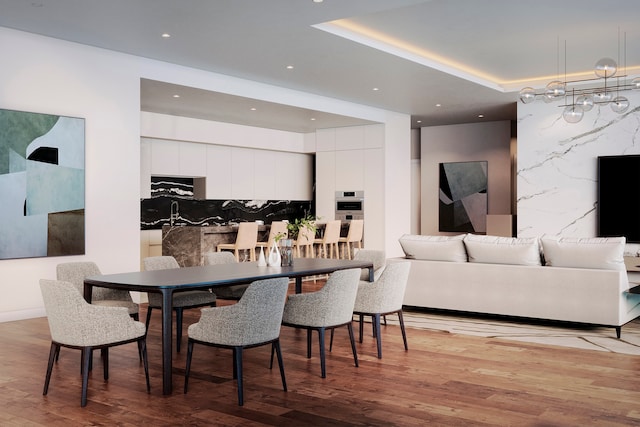 dining area with a raised ceiling, light wood-type flooring, and an inviting chandelier