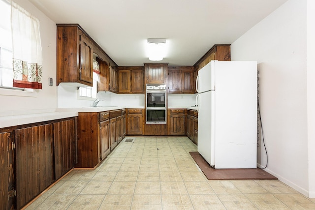 kitchen with white refrigerator, dark brown cabinetry, light tile floors, double oven, and sink