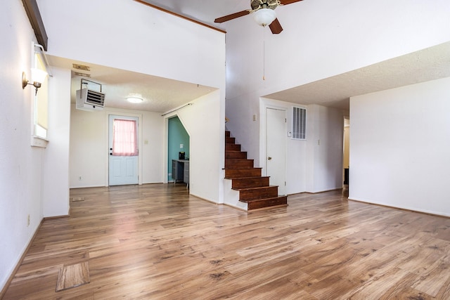 interior space featuring ceiling fan, an AC wall unit, light hardwood / wood-style flooring, and a towering ceiling