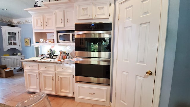 kitchen featuring light stone counters, stainless steel appliances, light tile floors, crown molding, and white cabinets