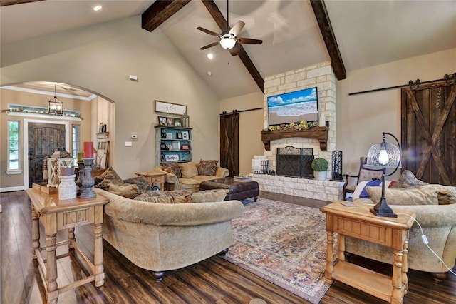 living room with beam ceiling, a barn door, a fireplace, ceiling fan, and dark hardwood / wood-style flooring