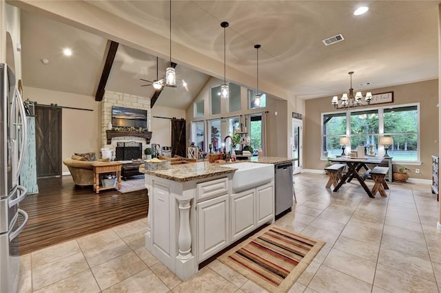 kitchen with an island with sink, a fireplace, sink, a barn door, and white cabinets