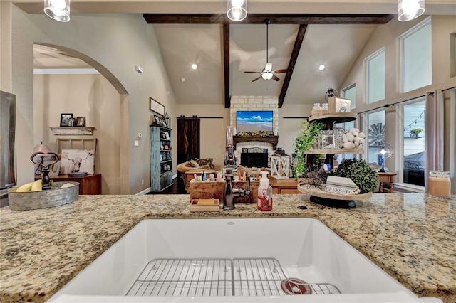 kitchen with high vaulted ceiling, beam ceiling, ceiling fan, and light stone countertops