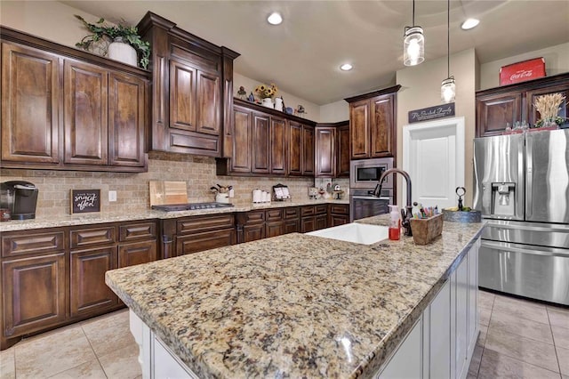 kitchen featuring backsplash, a center island with sink, stainless steel appliances, and decorative light fixtures