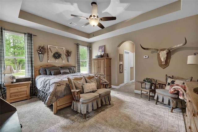 carpeted bedroom with ceiling fan, multiple windows, and a raised ceiling