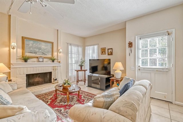 tiled living room with a brick fireplace, a textured ceiling, and ceiling fan