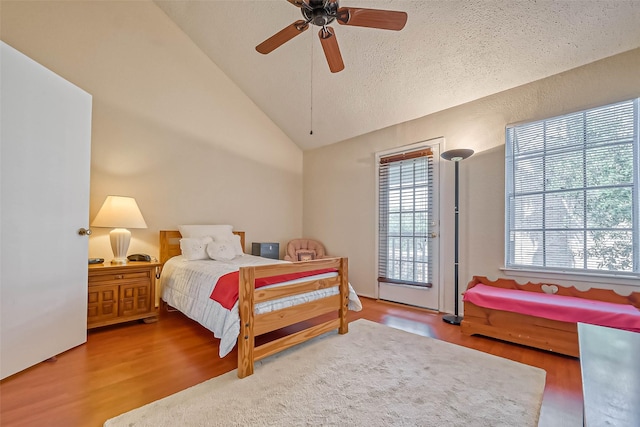 bedroom with ceiling fan, lofted ceiling, access to outside, wood-type flooring, and a textured ceiling