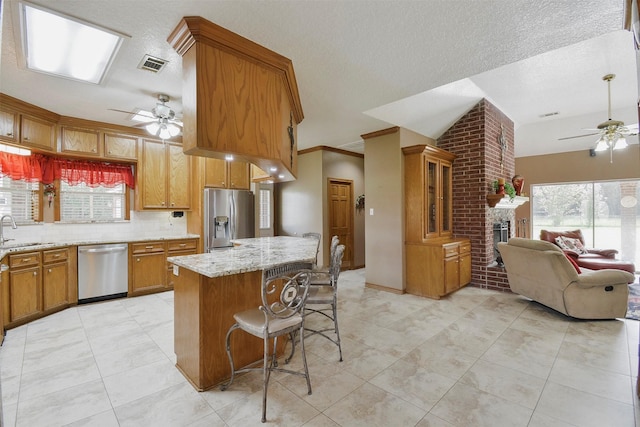 kitchen with a kitchen breakfast bar, stainless steel appliances, ceiling fan, and light stone counters