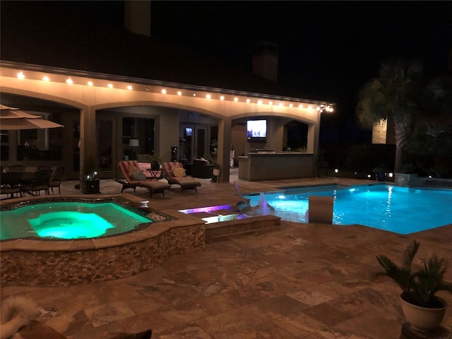 pool at night featuring a patio area and an in ground hot tub