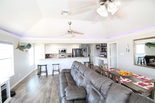 living room with ceiling fan, ornamental molding, light wood-type flooring, and a raised ceiling