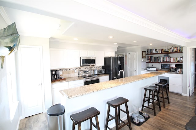 kitchen featuring a kitchen island, a breakfast bar area, appliances with stainless steel finishes, white cabinetry, and dark hardwood / wood-style floors