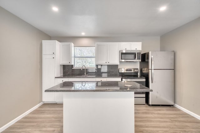 kitchen with dark stone counters, white cabinets, light hardwood / wood-style floors, stainless steel appliances, and a center island