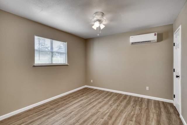 empty room with ceiling fan, light wood-type flooring, and a wall unit AC