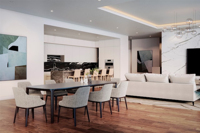 dining space featuring a notable chandelier, a raised ceiling, and light hardwood / wood-style flooring