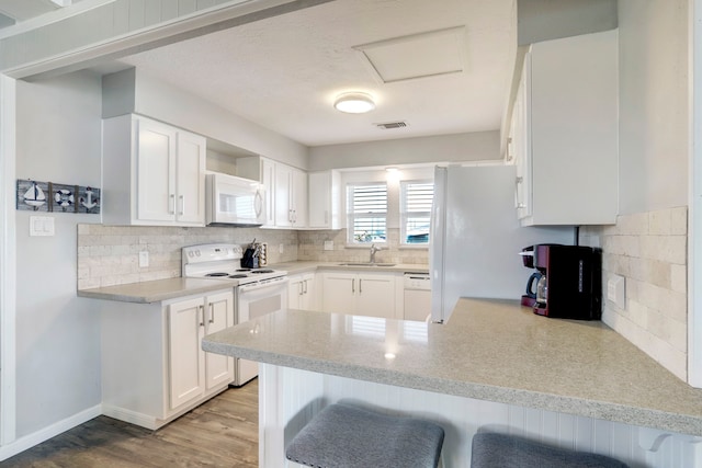 kitchen featuring kitchen peninsula, white appliances, a kitchen breakfast bar, wood-type flooring, and sink