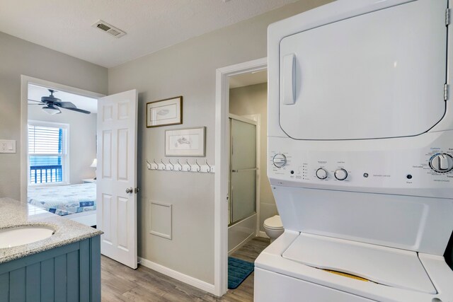 laundry area featuring stacked washer and dryer, ceiling fan, sink, and light wood-type flooring