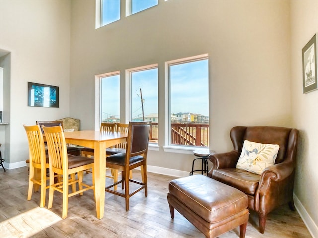 dining space with light hardwood / wood-style flooring, a wealth of natural light, and a towering ceiling