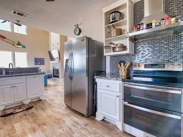 kitchen featuring stainless steel appliances, light hardwood / wood-style flooring, white cabinets, backsplash, and dark stone countertops