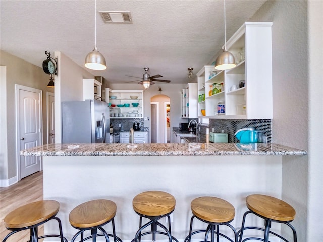 kitchen with ceiling fan, light stone countertops, white cabinetry, and stainless steel fridge with ice dispenser