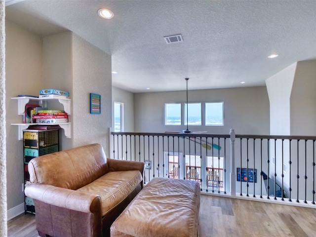 sitting room with ceiling fan, a wealth of natural light, hardwood / wood-style flooring, and a textured ceiling