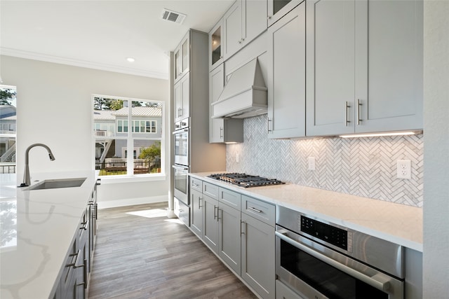 kitchen with stainless steel appliances, hardwood / wood-style flooring, custom exhaust hood, light stone counters, and sink