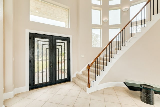 entrance foyer featuring a towering ceiling, light tile floors, and french doors