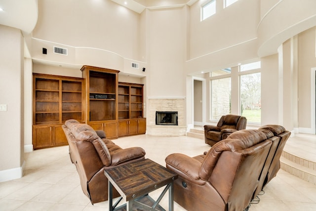 tiled living room featuring a stone fireplace and a high ceiling