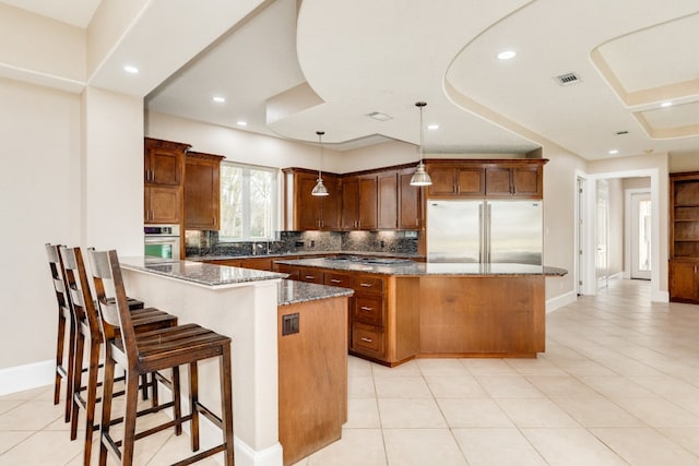 kitchen featuring a kitchen breakfast bar, light tile flooring, appliances with stainless steel finishes, and dark stone countertops