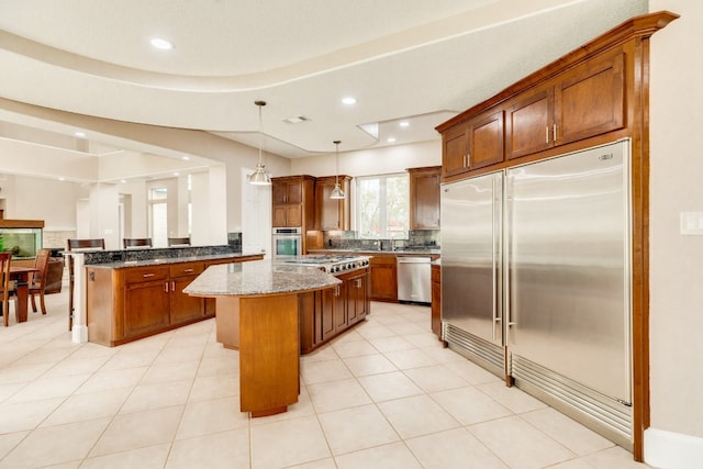 kitchen featuring decorative light fixtures, a kitchen island, tasteful backsplash, appliances with stainless steel finishes, and dark stone countertops