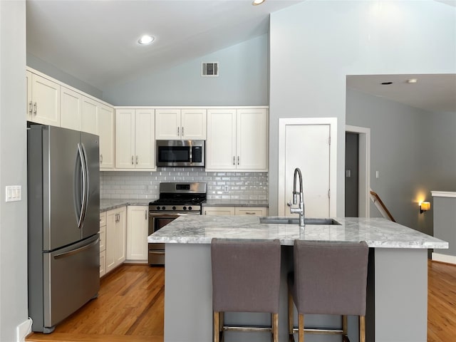 9822 Samantha Suzanne Ct, Houston, TX 77025 - kitchen featuring appliances with stainless steel finishes, tasteful backsplash, light stone counters, an island with sink, and light hardwood / wood-style floors