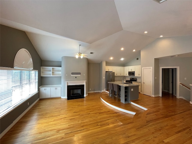 unfurnished living room with a tiled fireplace, ceiling fan, high vaulted ceiling, light hardwood / wood-style floors, and built in shelves