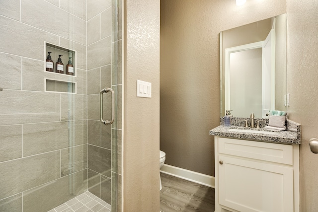 bathroom with hardwood / wood-style floors, vanity, toilet, and a shower with shower door