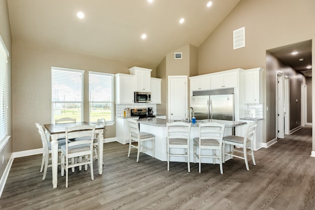 kitchen with white cabinets, appliances with stainless steel finishes, a center island with sink, and light stone countertops