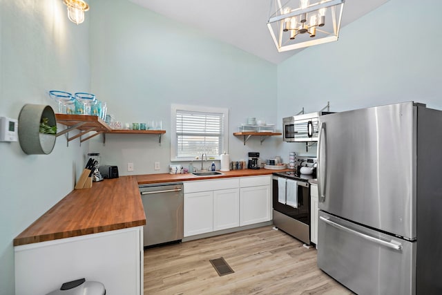 kitchen with wooden counters, appliances with stainless steel finishes, white cabinets, light wood-type flooring, and sink