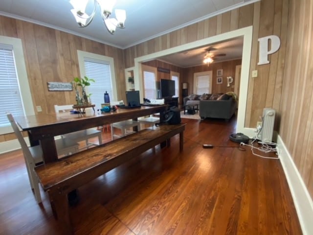 dining area featuring ornamental molding, dark hardwood / wood-style flooring, radiator, wood walls, and ceiling fan with notable chandelier