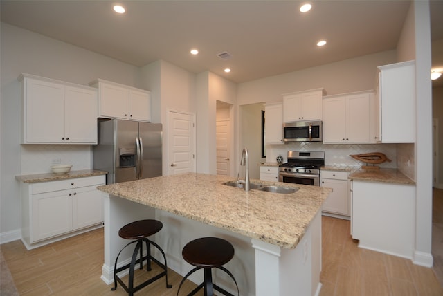 kitchen with an island with sink, white cabinets, appliances with stainless steel finishes, backsplash, and a breakfast bar area