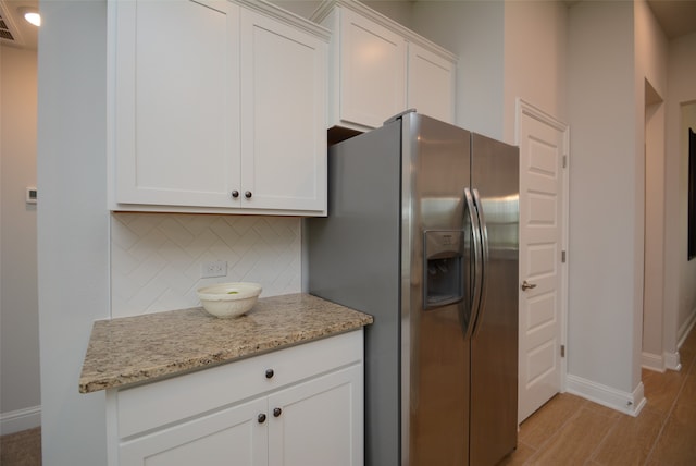 kitchen with tasteful backsplash, light stone counters, white cabinetry, and stainless steel refrigerator with ice dispenser