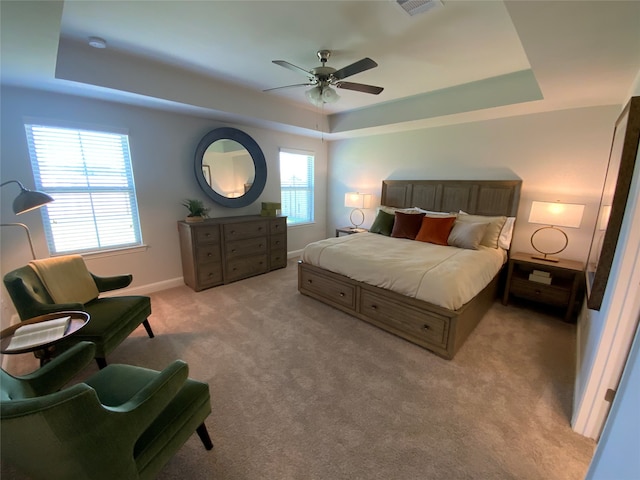 carpeted bedroom with ceiling fan and a tray ceiling