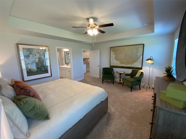 bedroom with light carpet, ensuite bathroom, ceiling fan, and a tray ceiling