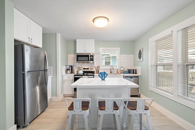 kitchen with a kitchen island, backsplash, stainless steel appliances, white cabinetry, and light wood-type flooring