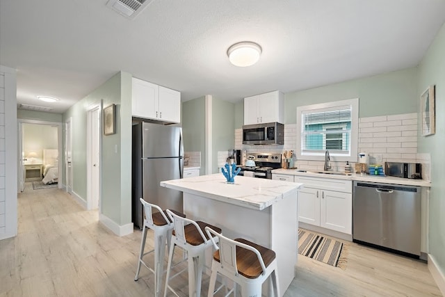 kitchen featuring appliances with stainless steel finishes, backsplash, light hardwood / wood-style flooring, and white cabinets
