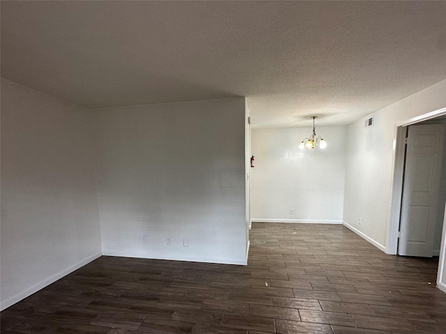 empty room featuring dark hardwood / wood-style floors, a textured ceiling, and an inviting chandelier