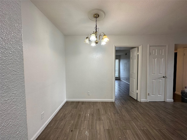 empty room with dark wood-type flooring and an inviting chandelier