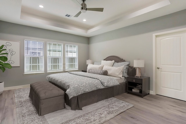 bedroom featuring ceiling fan, a raised ceiling, and light wood-type flooring