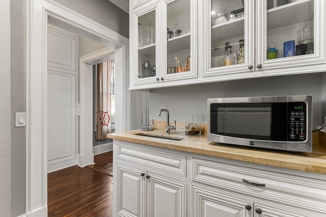 bar featuring dark hardwood / wood-style floors, light stone countertops, white cabinetry, and sink