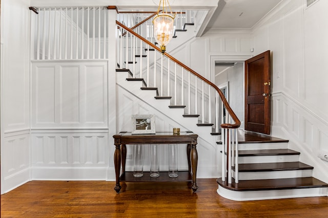 stairway with crown molding, a notable chandelier, and dark wood-type flooring