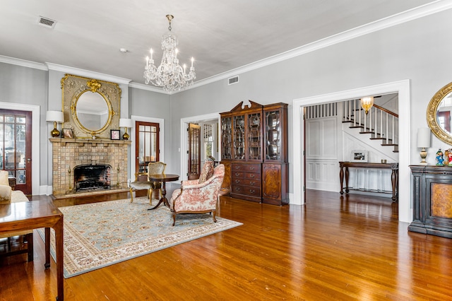 living room with an inviting chandelier, hardwood / wood-style floors, ornamental molding, and a brick fireplace