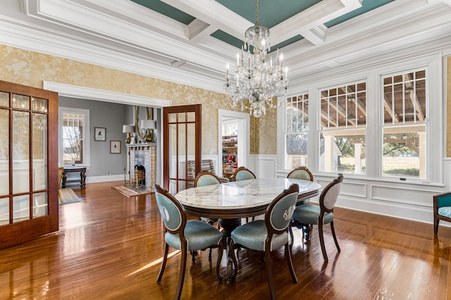 dining space with coffered ceiling, a brick fireplace, crown molding, dark hardwood / wood-style floors, and an inviting chandelier