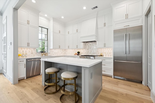 kitchen featuring appliances with stainless steel finishes, a sink, premium range hood, light wood-type flooring, and recessed lighting