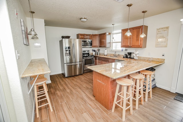 kitchen with kitchen peninsula, hanging light fixtures, appliances with stainless steel finishes, a breakfast bar, and light wood-type flooring